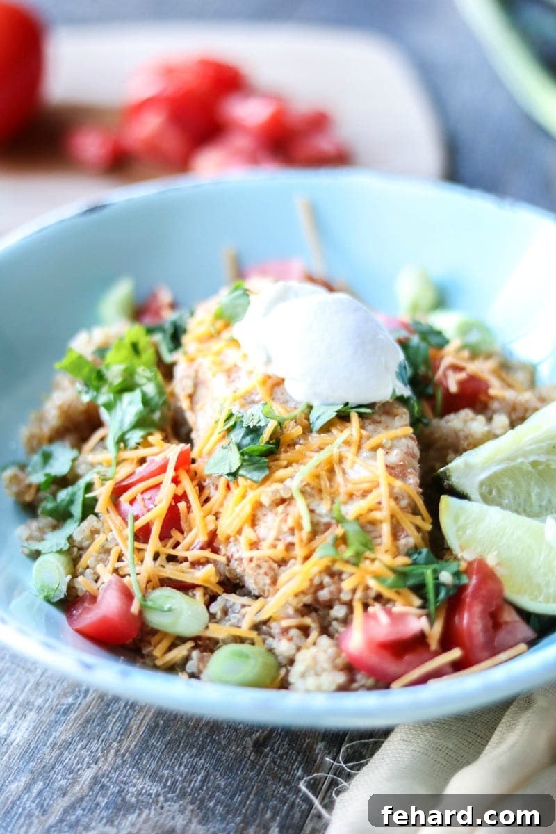 Chicken Fajita Quinoa Bowl A blue pottery bowl is filled with a delicious Tex-Mex inspired chicken fajita quinoa mix, topped with a perfectly cooked chicken breast and fresh garnishes.