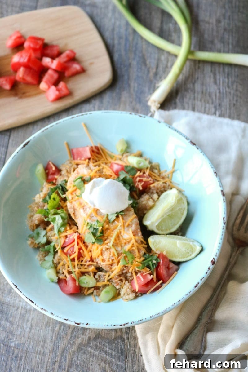 Chicken Burrito Fajita Bowl A vibrant blue bowl featuring Mexican-style quinoa, topped with shredded chicken, melted cheese, a dollop of sour cream, and fresh lime wedges.