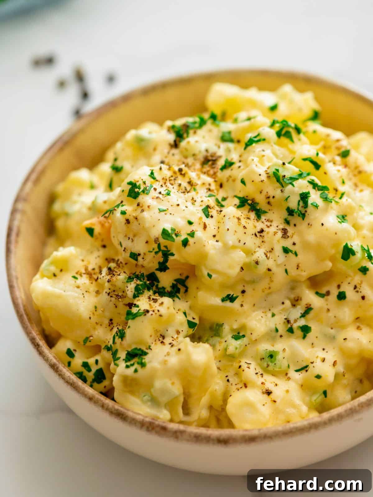 Large bowl of creamy Old-Fashioned Potato Salad garnished with fresh parsley and a sprinkle of crushed black pepper.