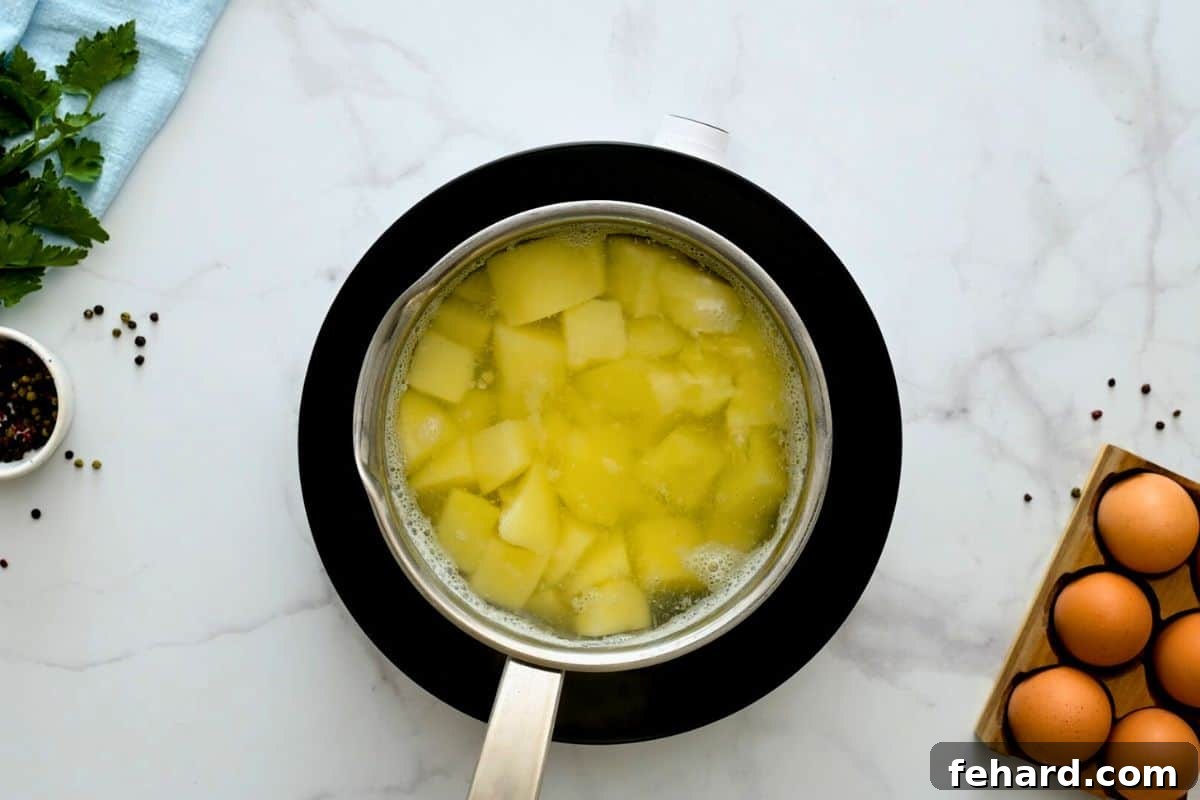 Peeled and diced russet potatoes simmering in a large saucepan of salted cold water.