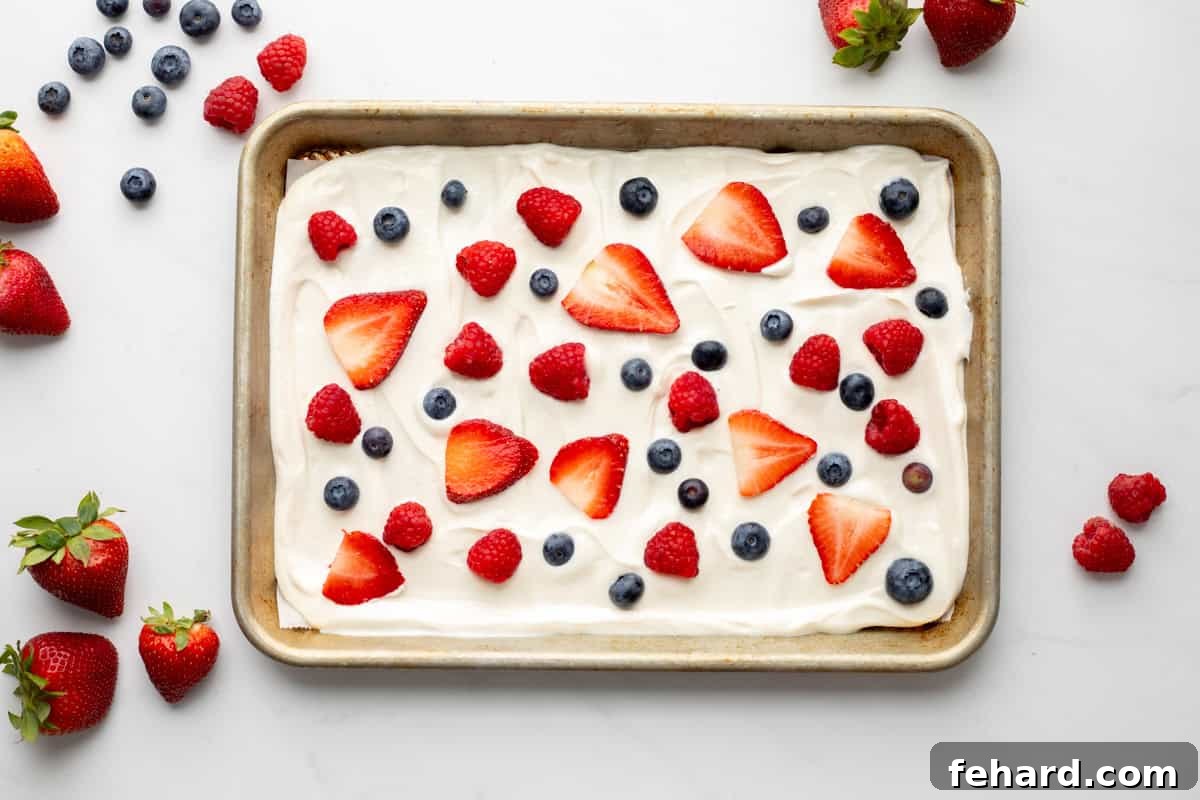 Yogurt Bark Freezing Yogurt spread on baking sheet that has been lined with parchment paper topped with strawberries, raspberries, and blueberries.