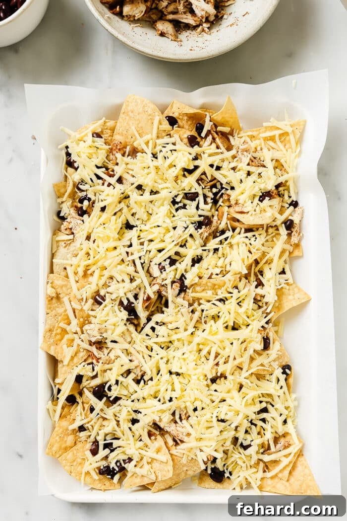 An overhead view of rotisserie chicken nachos on a sheet pan before going into the oven. 