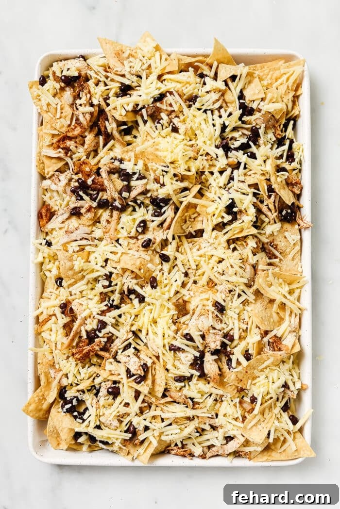 An overhead view of layered sheet pan nachos before going into the oven. 