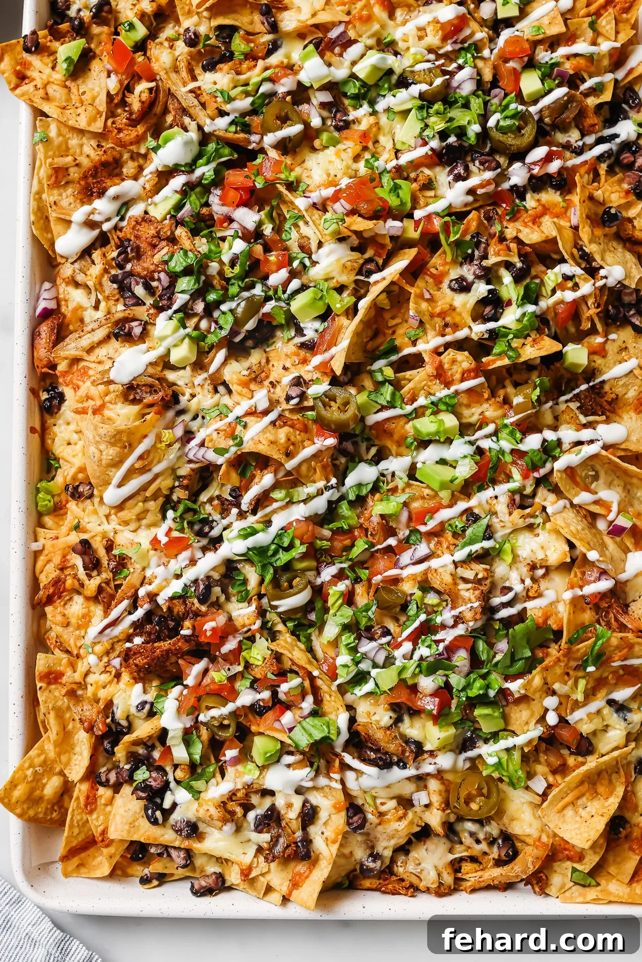 An overhead view of loaded rotisserie chicken nachos with sour cream, cilantro, and pico de gallo. 