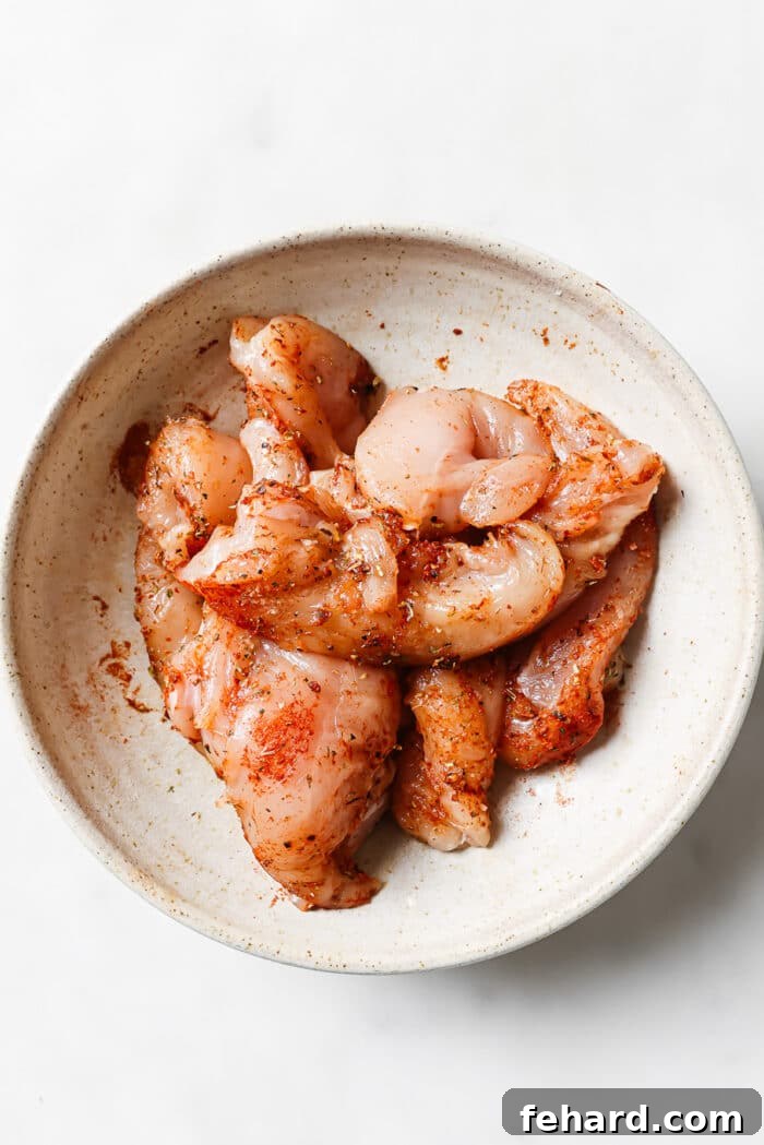 An overhead view of seasoned chicken tenders in a large mixing bowl. 