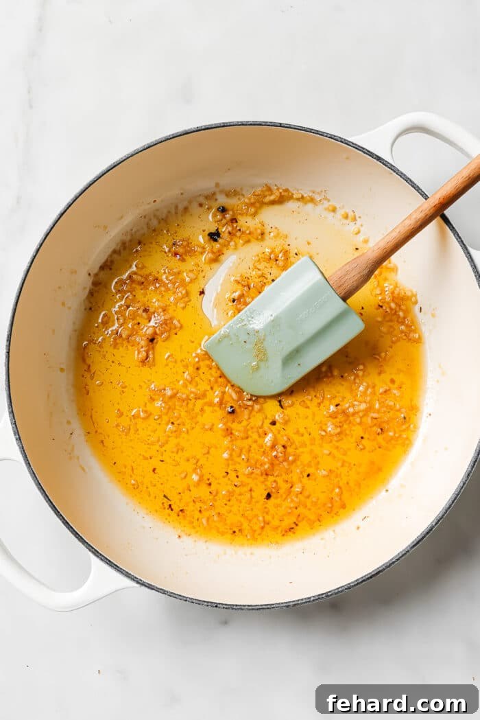 A large ceramic cast-iron pan with a blue spatula, butter, and garlic in it. 