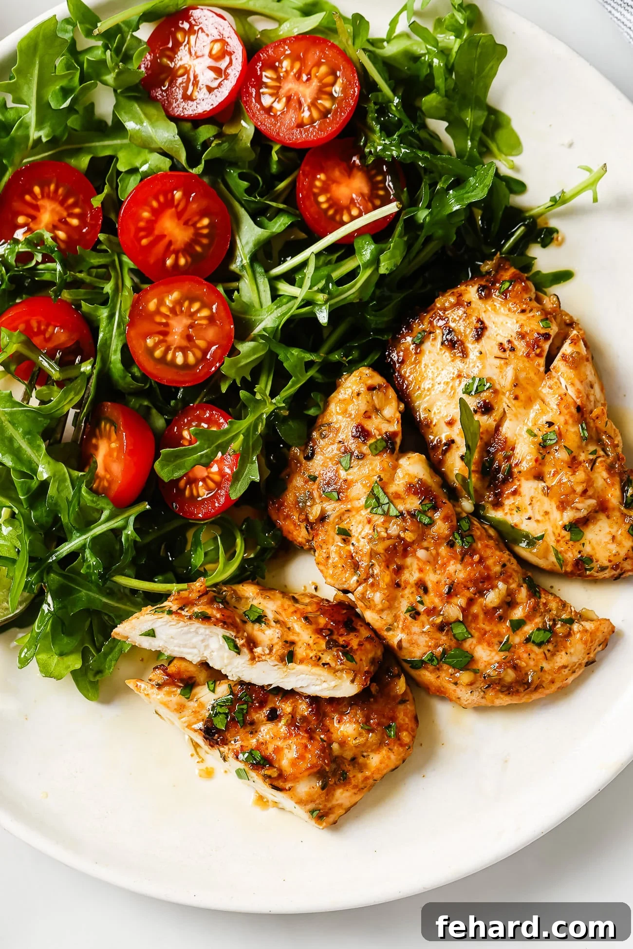 Garlic butter chicken tenders next to a side salad on a white plate.