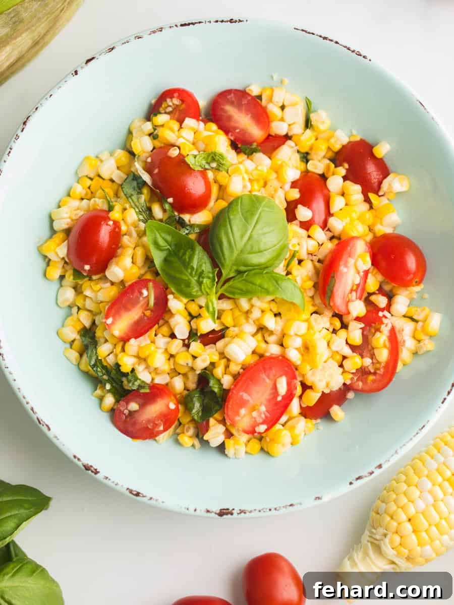 Vibrant fresh corn and tomato salad with basil in a rustic blue bowl, with corn cobs and grape tomatoes scattered on a wooden counter, evoking a summer kitchen scene.