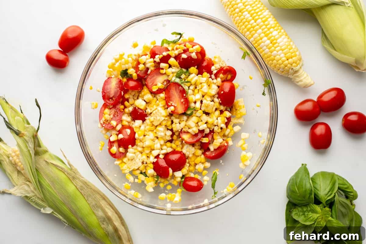 A large mixing bowl filled with vibrant corn kernels, halved tomatoes, and fresh basil leaves, all mixed together and glistening with dressing, ready to be served as a summer salad.