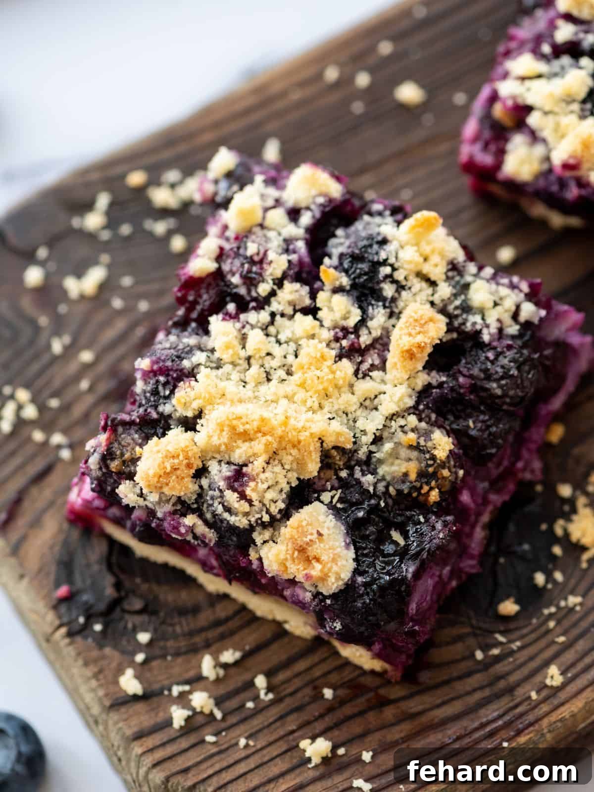 Perfectly sliced blueberry pie bars arranged on a rustic wooden cutting board, clearly showing the distinct layers of the golden shortbread crust, creamy purple blueberry filling, and a generous, buttery crumble topping.