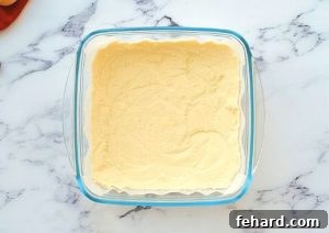 A golden, pre-baked shortbread crust resting in a glass 8x8 baking dish, ready to receive the blueberry filling.