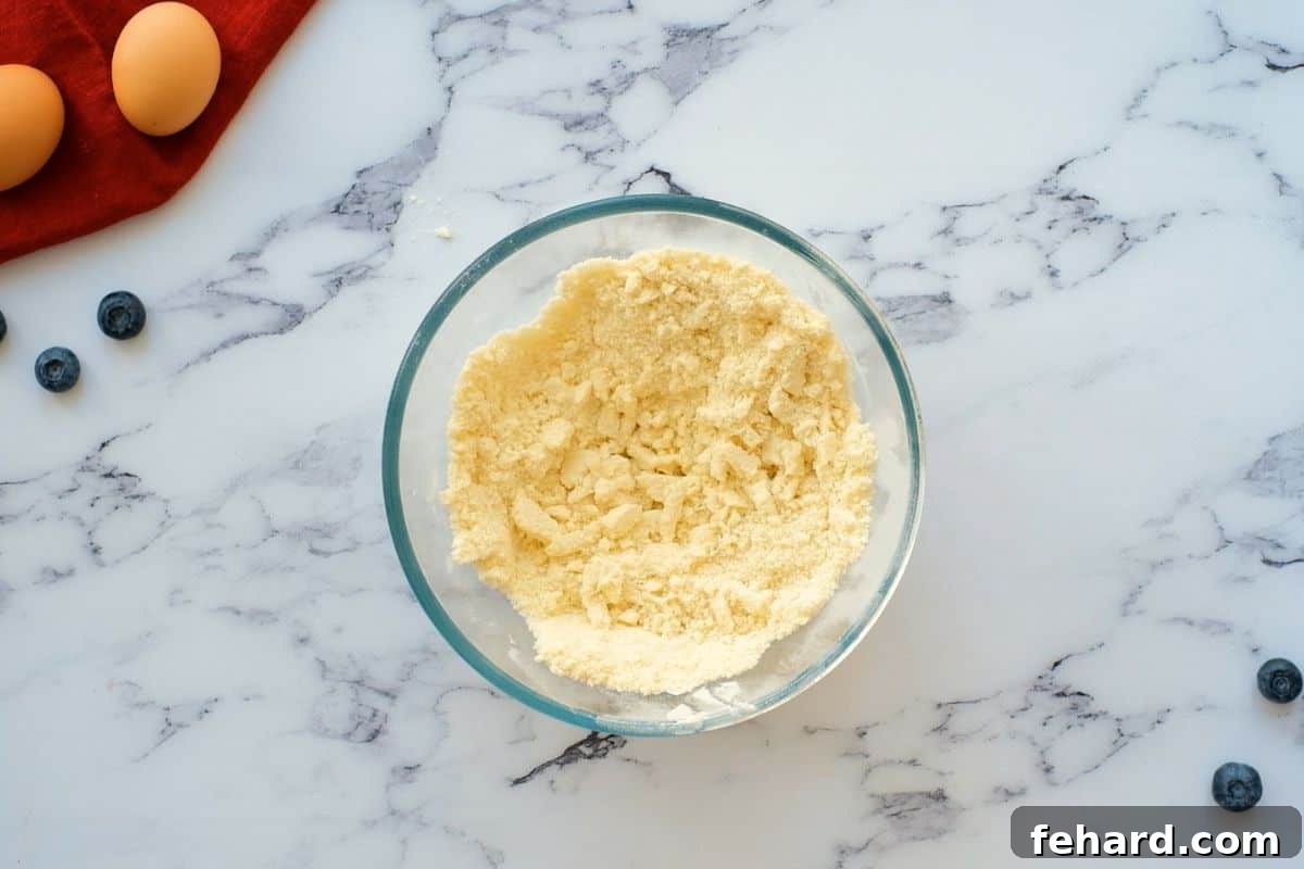 Cold butter cubes being mixed into flour and sugar until a uniform crumbly texture is formed, which will be divided for the crust and topping of the blueberry pie bars.
