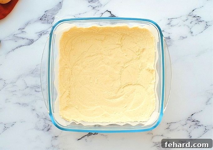 A perfectly formed and lightly golden shortbread crust pressed into a glass baking dish after being pre-baked, ready for the blueberry filling.