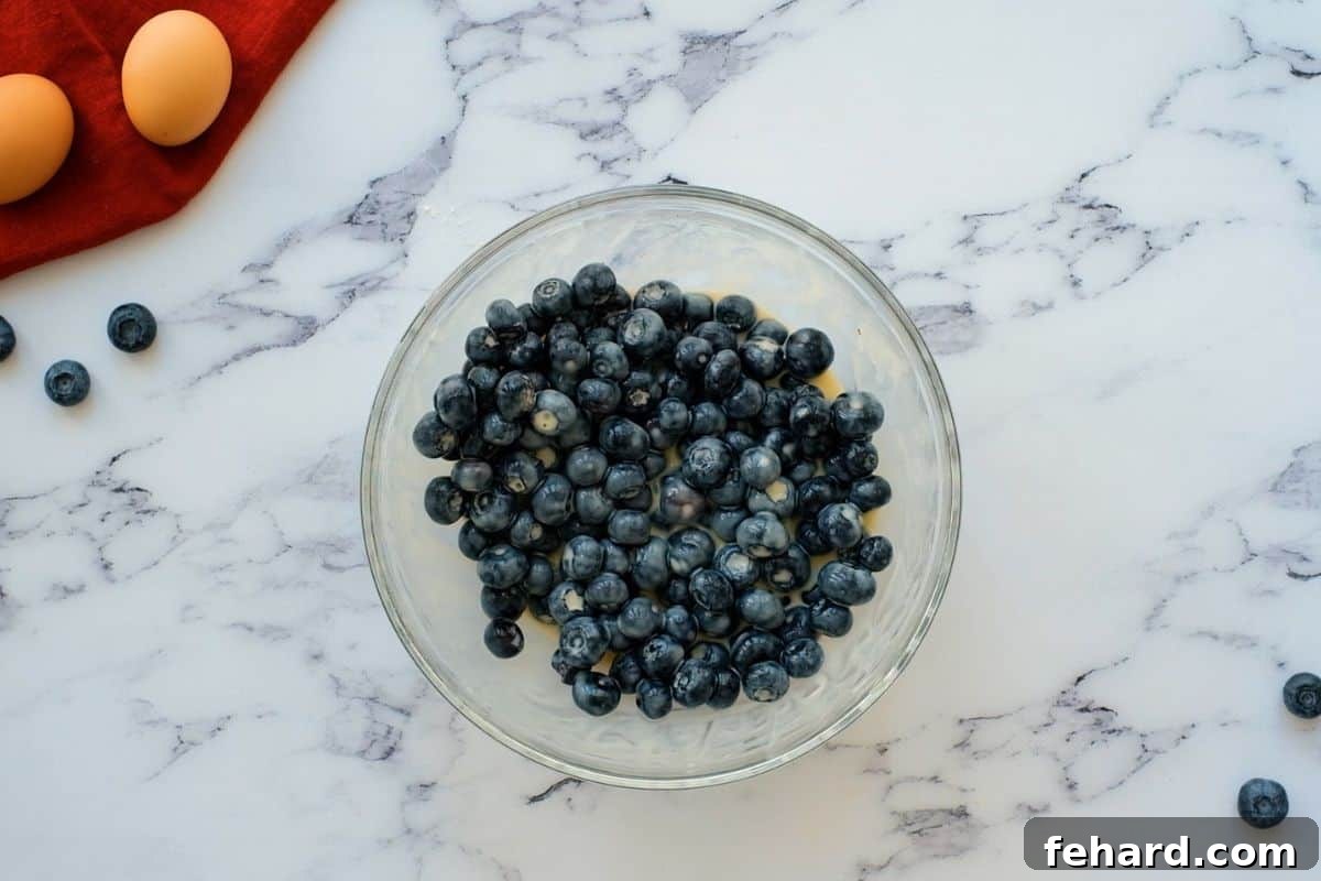 Vibrant fresh blueberries being gently folded into a bowl of creamy, sweetened sour cream mixture with an egg, creating the rich and colorful filling for the pie bars.