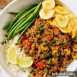 Overhead view of a delicious Picadillo recipe served in a white bowl with green beans and rice on the side.