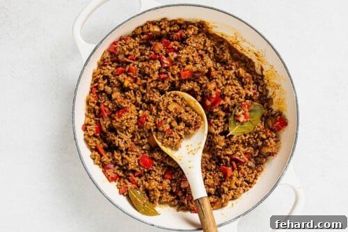 Picadillo simmering in a white skillet, with ground beef, vegetables, tomato sauce, and spices blending together.