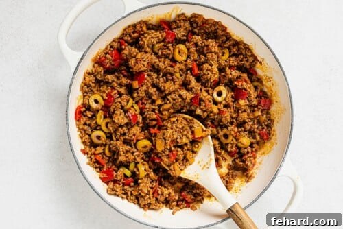 Picadillo with green olives stirred in, gently simmering in a white skillet, nearly ready to be served.