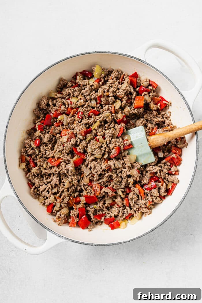Adding ground beef to the skillet, cooking it alongside the aromatic sautéed vegetables until thoroughly browned and crumbled.