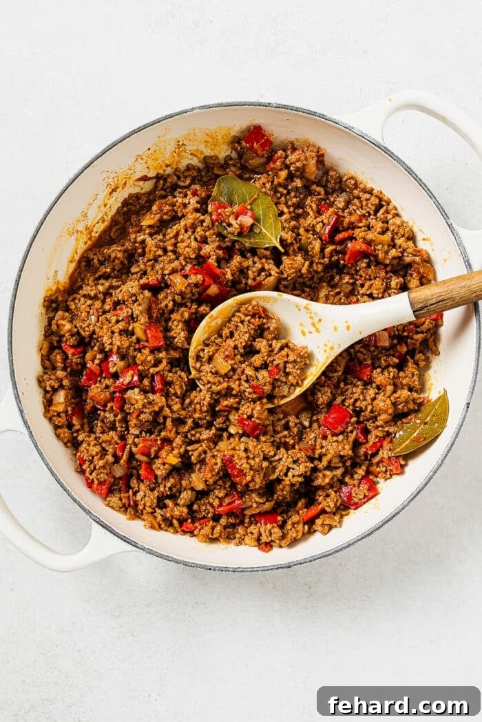 Pouring rich tomato sauce and savory beef broth into the skillet with browned ground beef and vegetables, along with various seasonings.