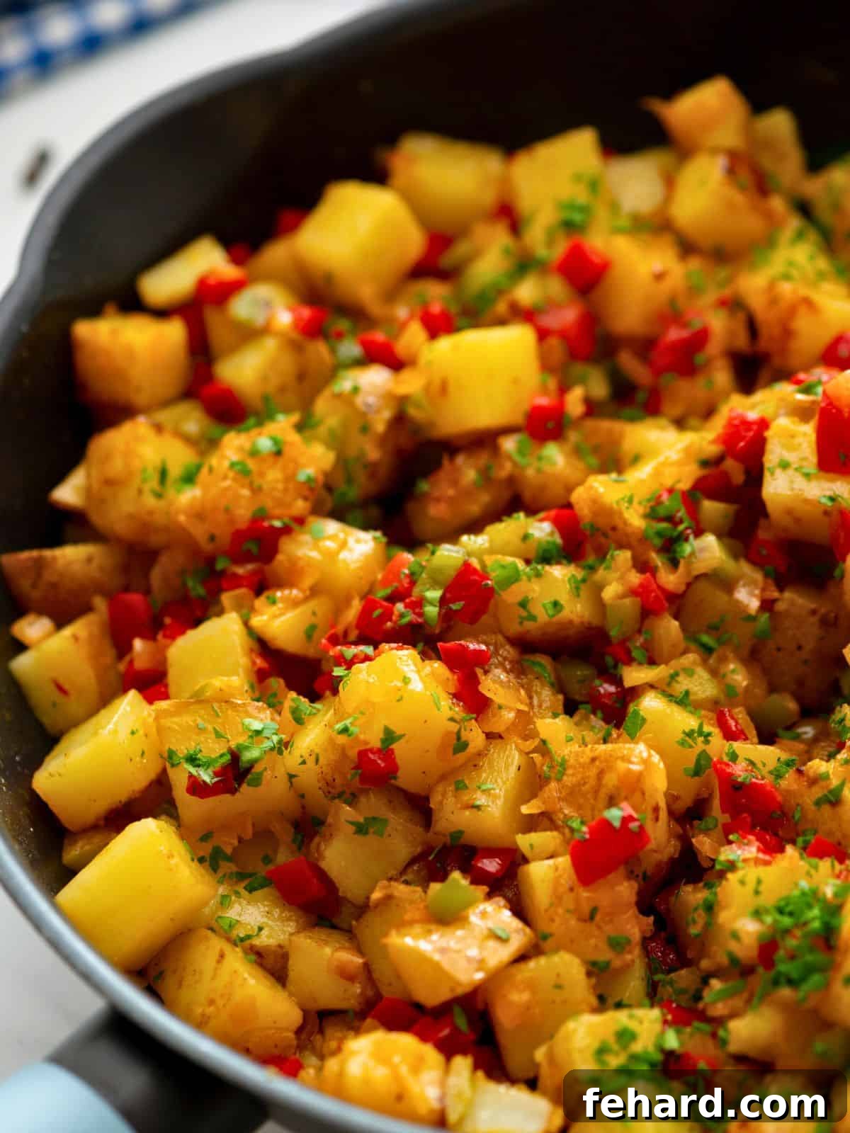Large skillet filled with golden pan-fried Potatoes O'Brien, mixed with vibrant red and green bell peppers and caramelized onions, garnished with fresh parsley.
