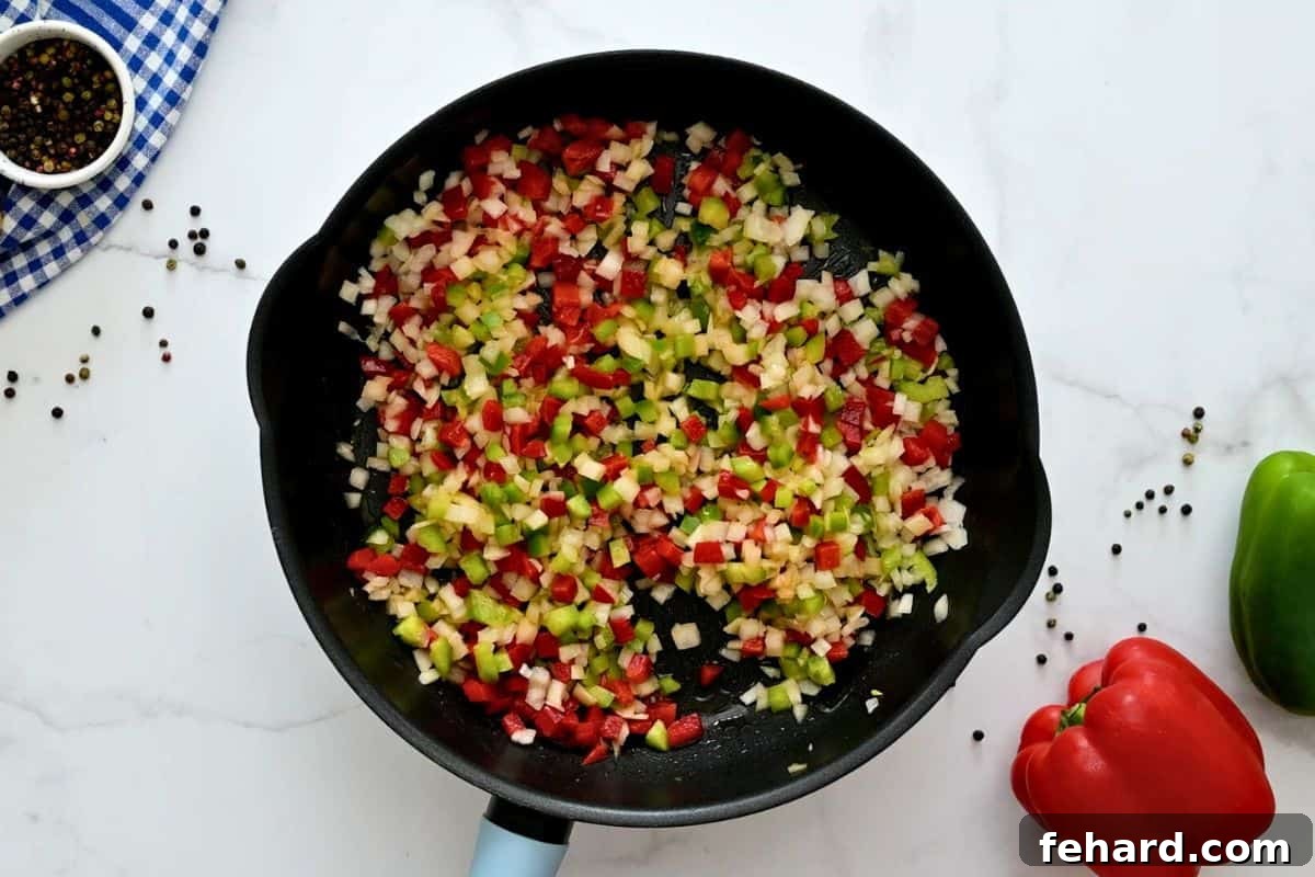 Finely chopped red and green bell peppers and yellow onions sautéing in a large skillet, glistening with oil and butter.