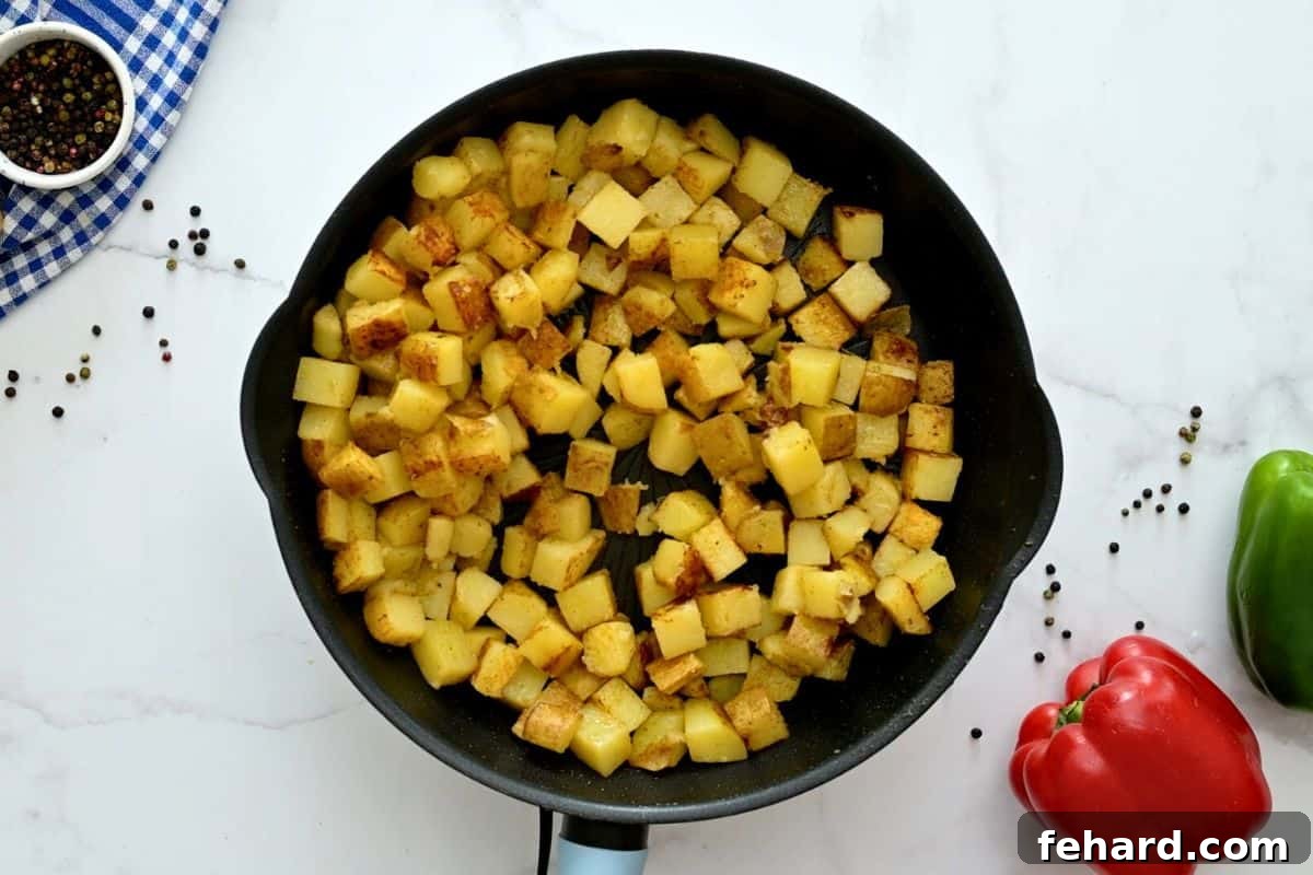 Cubed potatoes actively pan-frying in a large skillet, with visible steam and a developing golden-brown crust.
