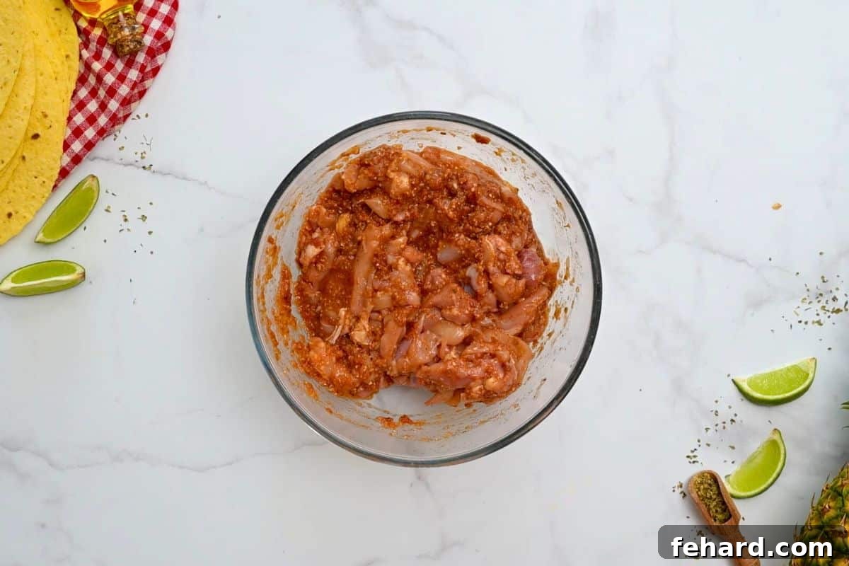 Thinly sliced chicken thighs submerged and tossed in a vibrant red al pastor marinade in a mixing bowl, ready for marination.