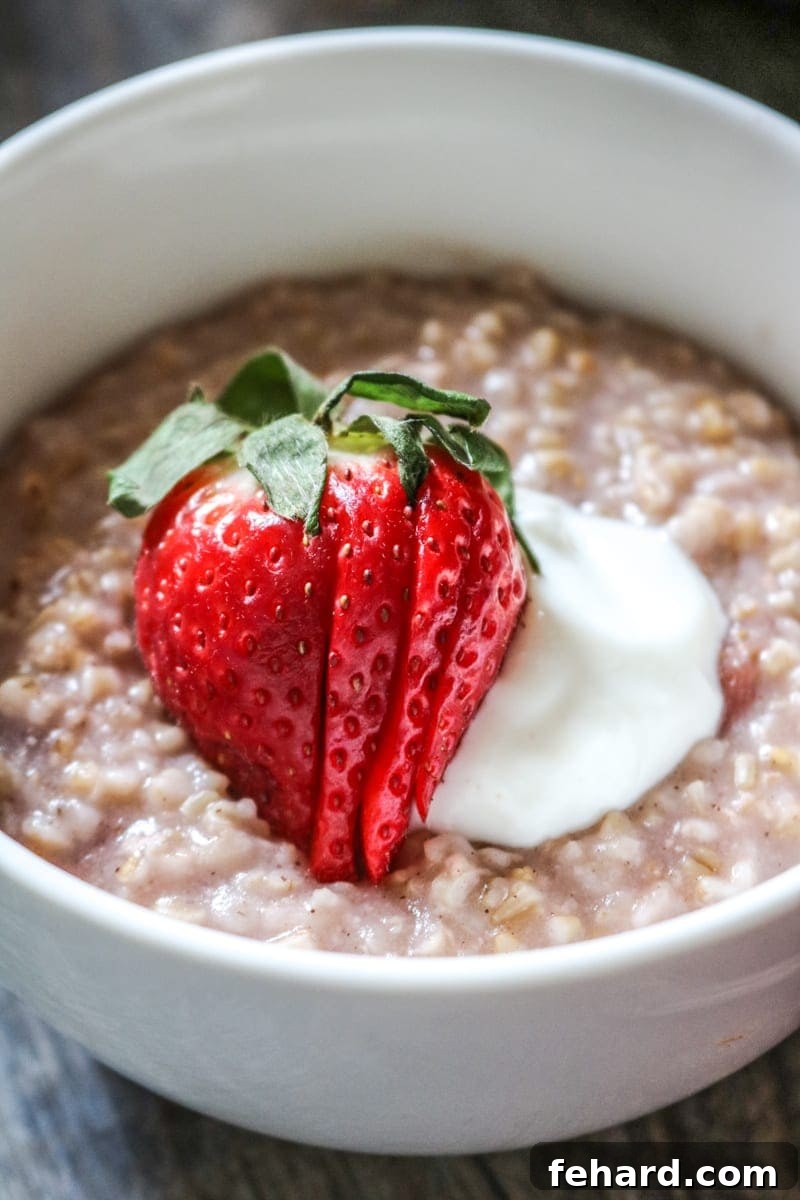Bowl of strawberry steel cut oats in white bowl topped with strawberries and yogurt. 