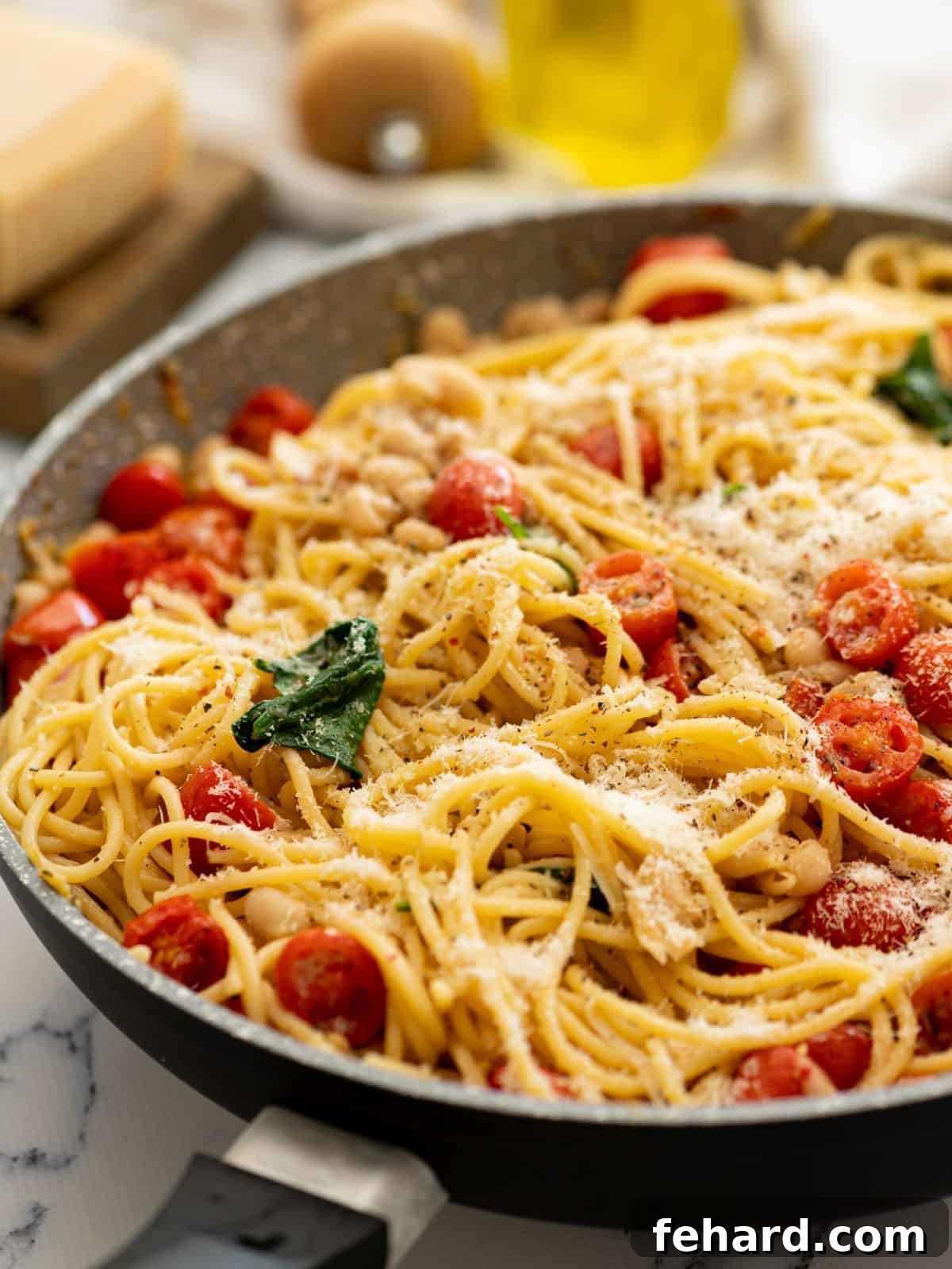 White Bean Pasta with Spinach and Tomatoes Large skillet filled with freshly made white bean pasta, featuring tender noodles, blistered cherry tomatoes, creamy white beans, and vibrant spinach, generously topped with grated Parmesan cheese.