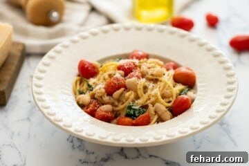 Quick White Bean Pasta with Burst Tomatoes and Fresh Spinach 10 Bowl of white bean pasta dished out in white bowl topped with parmesan cheese.
