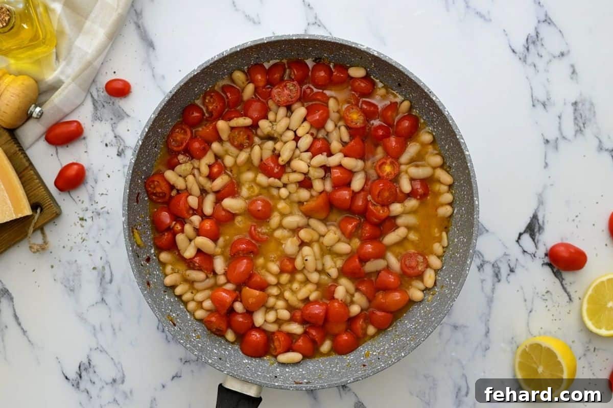 White Bean Pasta Base with Tomatoes and Beans Creamy white beans combined with blistered tomatoes and aromatic seasonings in a sauté pan, forming the rich base for white bean pasta.