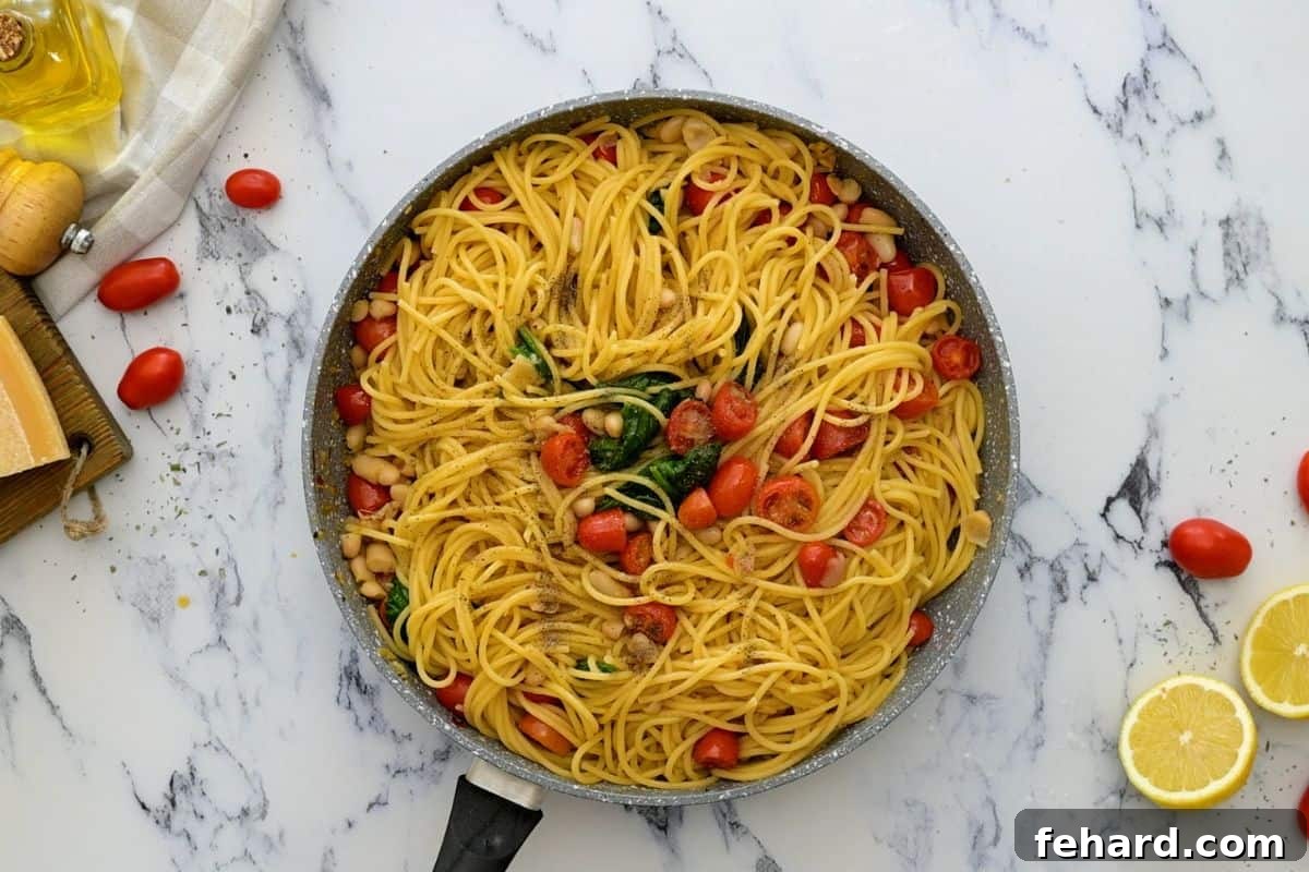 White Bean Pasta Tossed with Spinach and Tomatoes Cooked pasta being tossed with the tomato and white bean sauce in a large skillet, with fresh spinach just added.