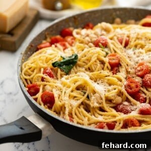Large skillet with pasta, white beans, tomatoes, and spinach topped with parmesan.