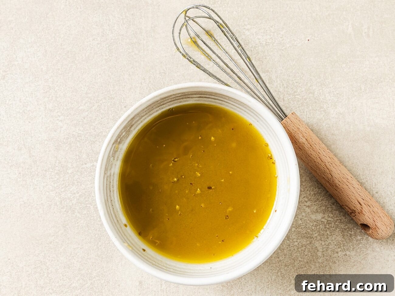Vibrant Italian Chopped Salad 4 A wooden whisk resting beside a bowl of freshly prepared vinaigrette salad dressing, highlighting the first step in making the salad.