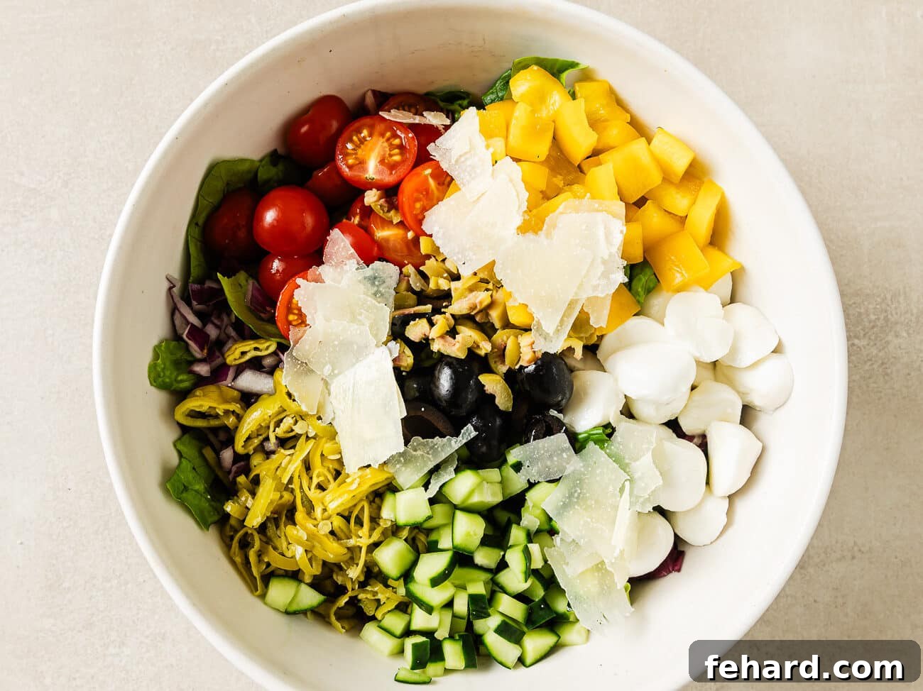 Vibrant Italian Chopped Salad 5 Various Italian chopped salad ingredients, including vegetables, cheeses, and olives, arranged neatly over a base of mixed lettuce in a large serving bowl.