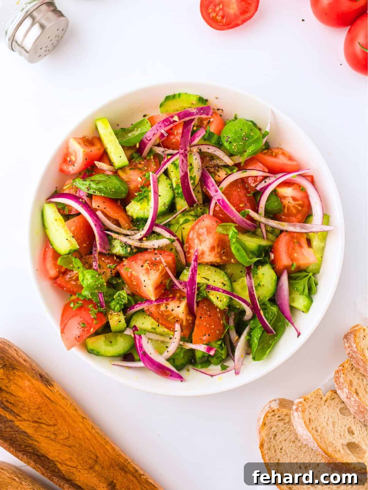 A close-up of a vibrant cucumber tomato salad in a white bowl, featuring sliced cucumbers, diced ripe tomatoes, thinly sliced red onions, and fresh basil leaves, all glistening with a simple Greek-inspired dressing. This image captures the freshness and appeal of a perfect summer salad.