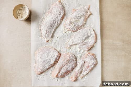 Raw chicken breast coated with flour on a countertop, seasoned and ready for cooking.