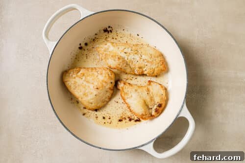 Chicken breast searing to a golden-brown in a skillet with sizzling butter and oil.