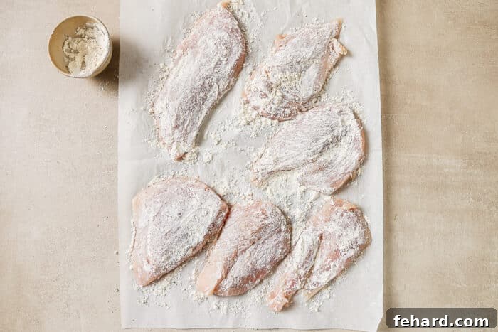 Six chicken cutlets coated in salt, pepper, and flour on a sheet of parchment paper, ready for searing.