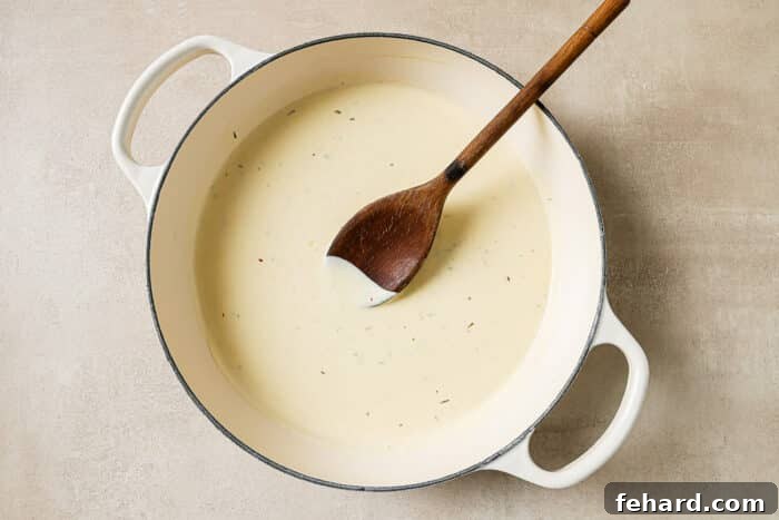 A creamy sauce simmering in the cast-iron Dutch oven, incorporating heavy cream, Parmesan, and seasonings after the garlic has been sautéed.