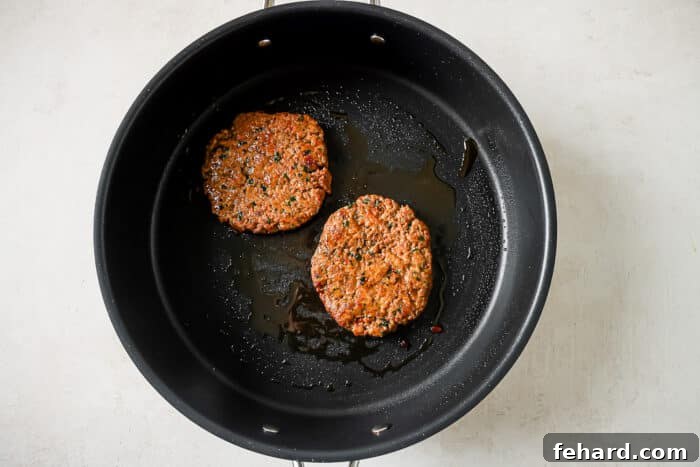 Healthy and Hearty Turkey Burger 7 Two ground turkey burger patties cooking in a large skillet.