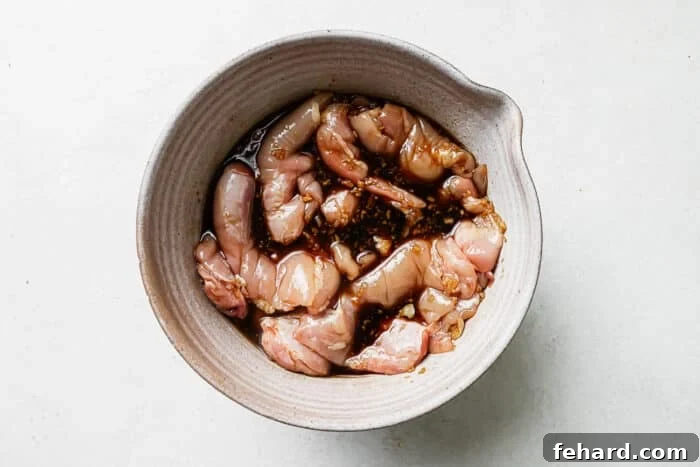 Chicken steeping in teriyaki marinade in a bowl.