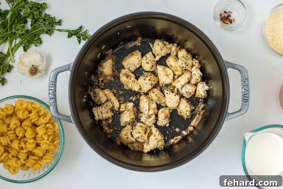 Searing Chicken for Garlic Parmesan Pasta Seared boneless skinless chicken breast chunks tossed in Italian seasoning in a Dutch oven, with uncooked pasta and cream waiting beside.