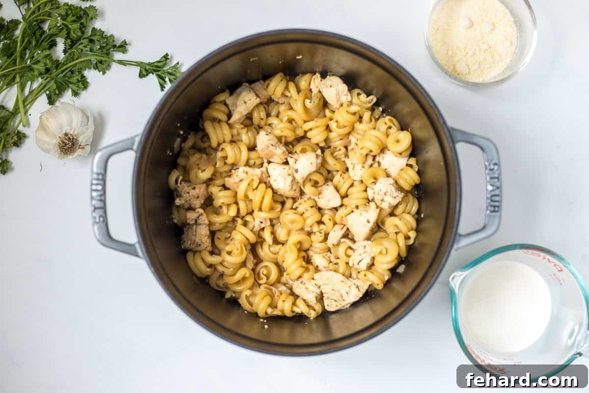 Simmering Pasta for Creamy Chicken Pasta Tender pasta and chicken simmering in a stock pan, absorbing the flavorful broth before the creamy ingredients are added.