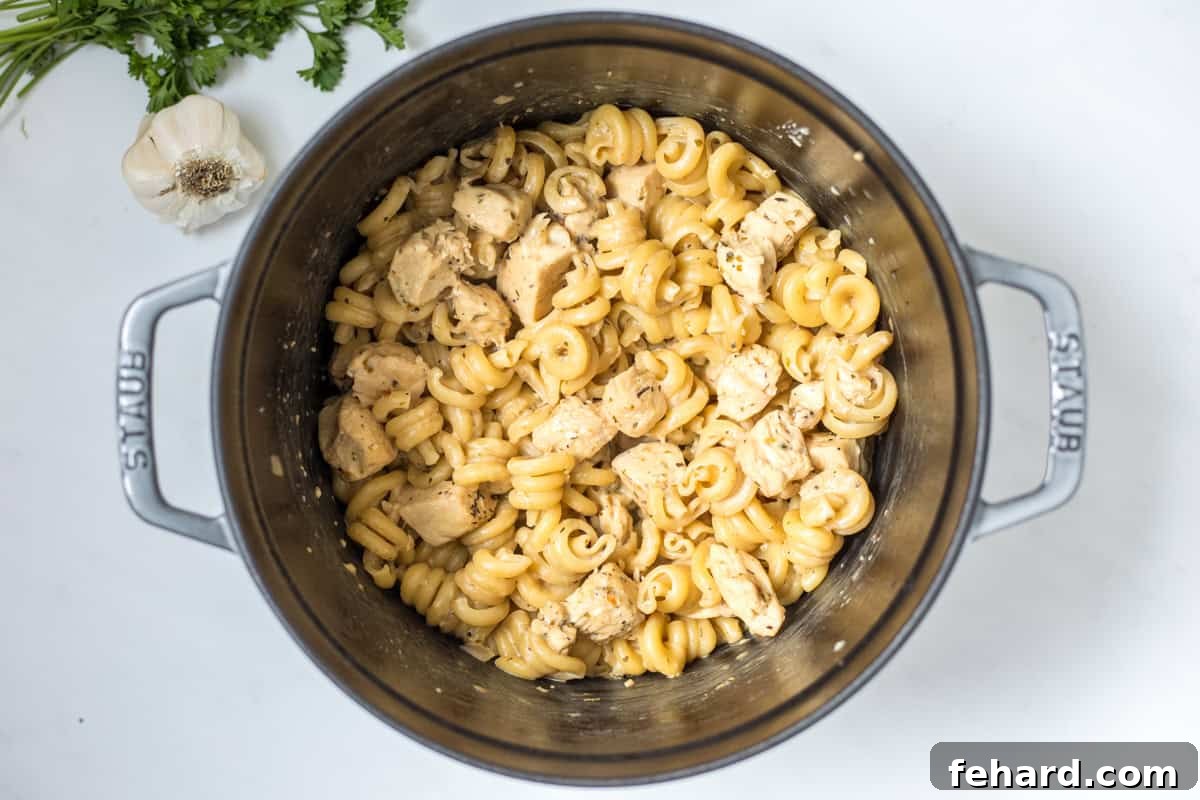 Adding Cream and Parmesan to Pasta Pasta in a large stock pan with chicken, generously coated in a rich, creamy parmesan sauce, adorned with fresh herbs.