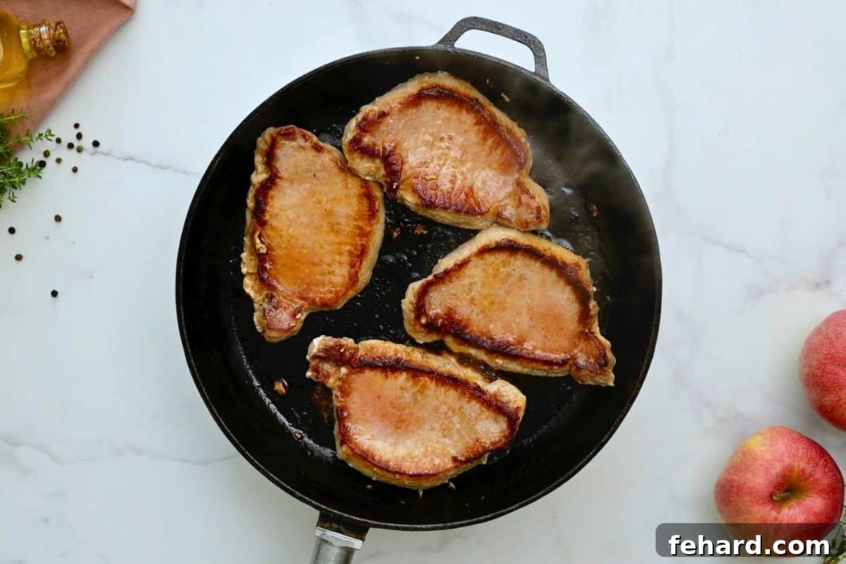 Perfectly Seared Pork Chops Ready for Sauce Four boneless pork loin chops arranged in a skillet after being perfectly seared to a golden-brown finish, showcasing a beautiful crust.
