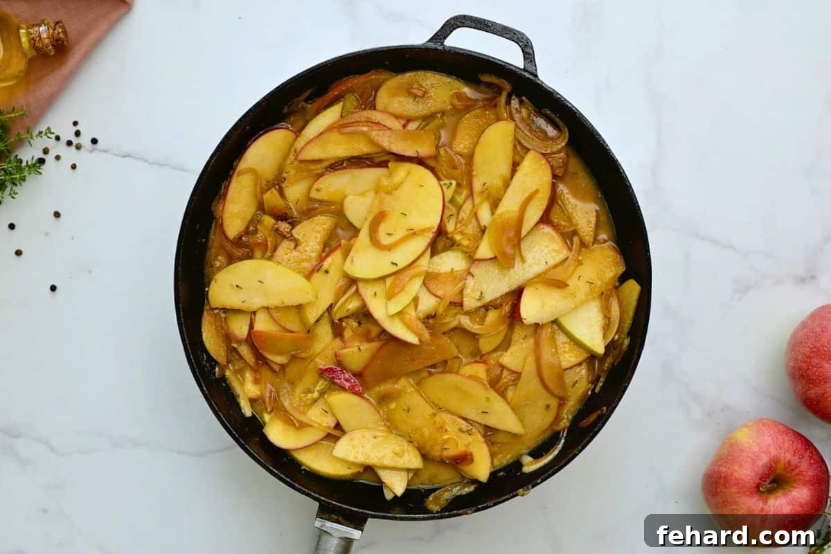 Apple Pork Chop Pan Sauce Creation Sautéed apples and onions simmering in a skillet with apple cider and fresh thyme, forming a rich and aromatic pan sauce.