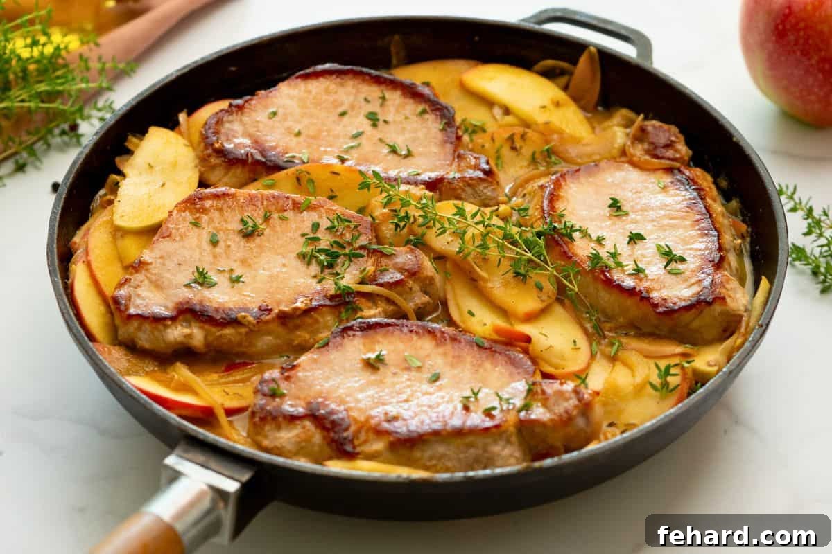 Pork Chops with Apples and Onions Completed Pan-seared pork chops nestled back into the skillet with sautéed apples and onions, simmering in the rich pan sauce, garnished with fresh thyme.
