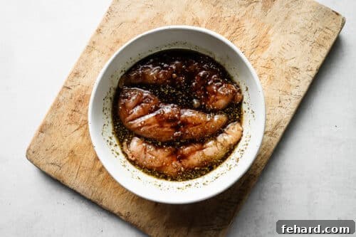 Balsamic marinade and raw chicken breast in a white bowl.