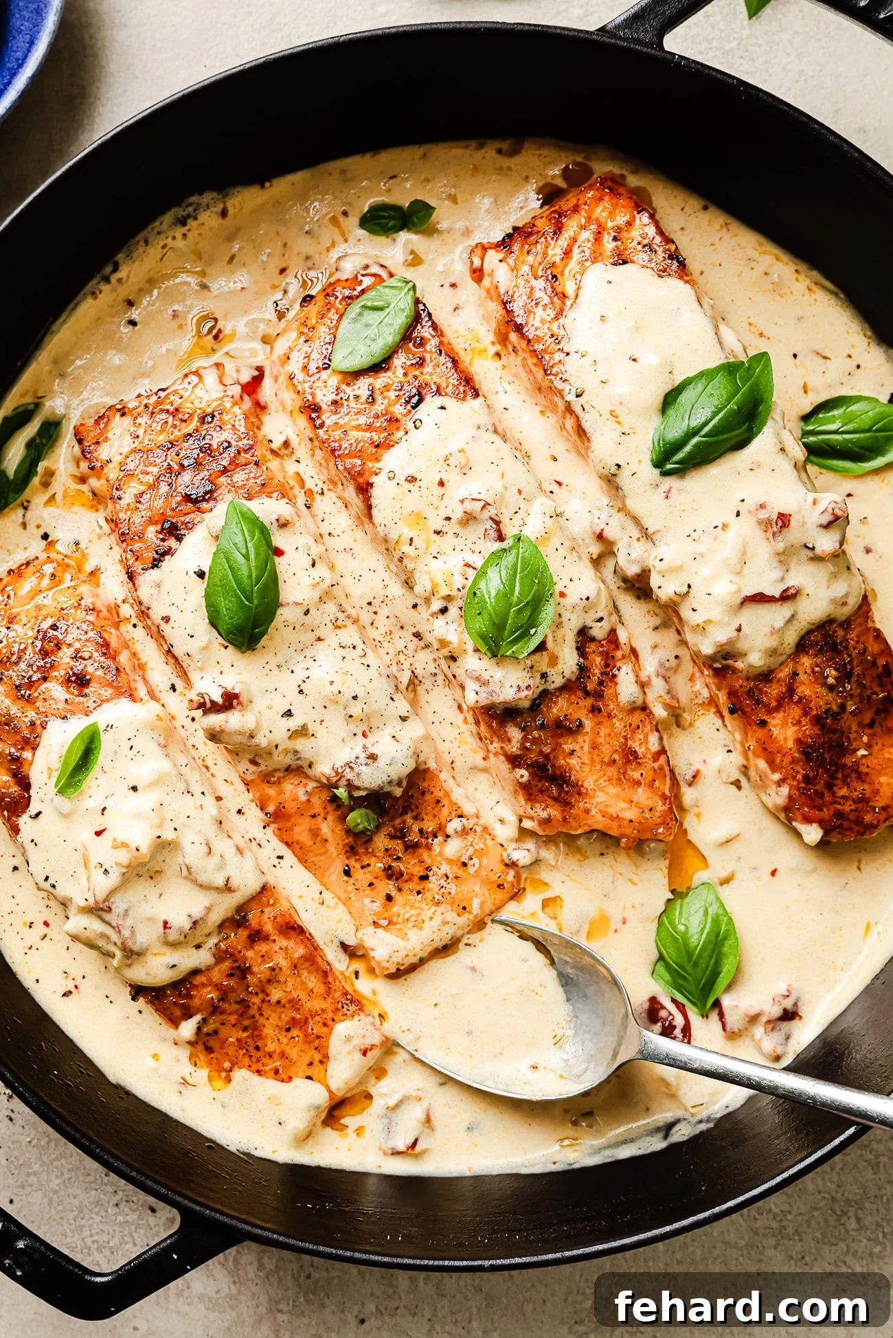 Overhead view of Marry Me Salmon in a cast-iron skillet, glistening with creamy sauce and fresh basil.